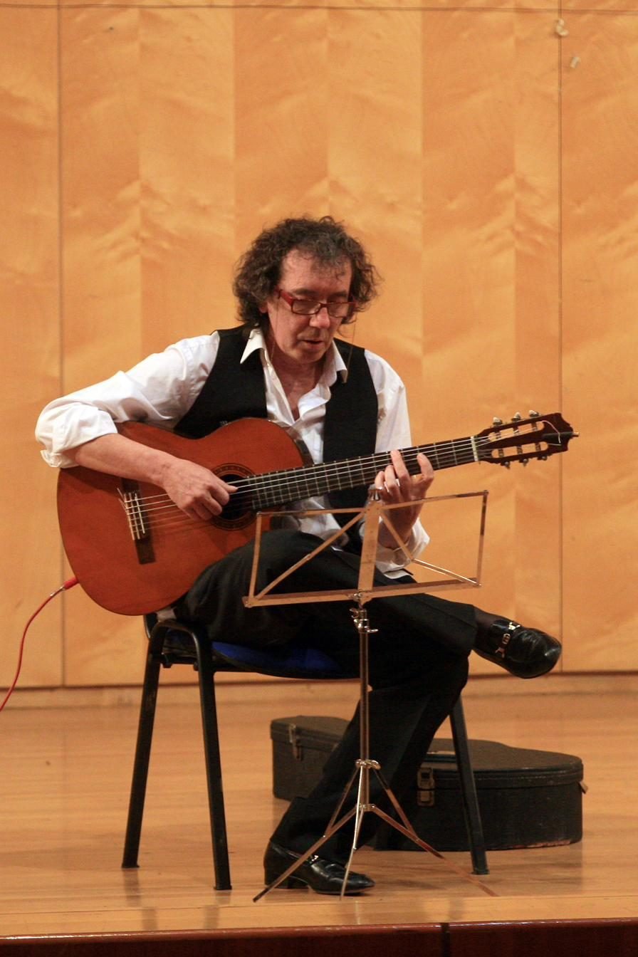 Miguel Anda tocando la guitarra sentado en el escenario de un auditorio