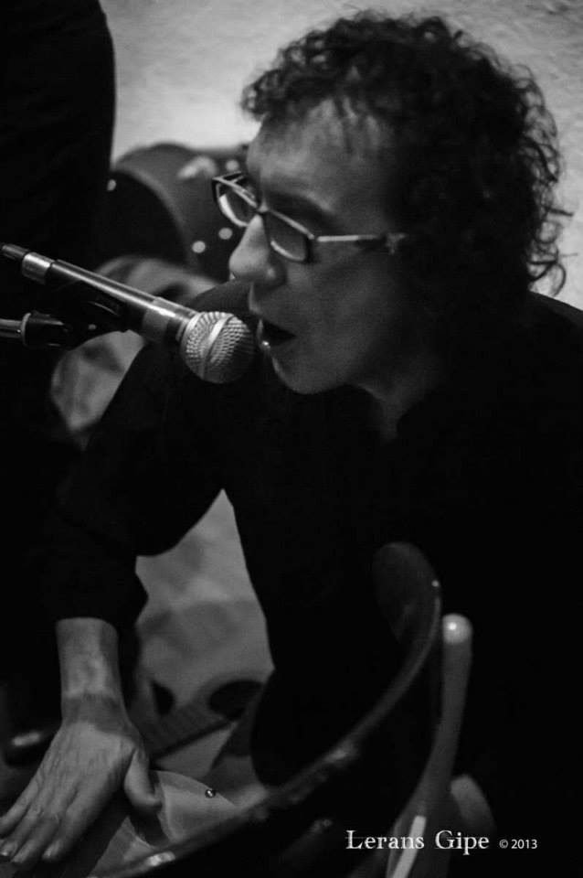 Miguel Anda cantando al micrófono mientras toca la percusión, en blanco y negro