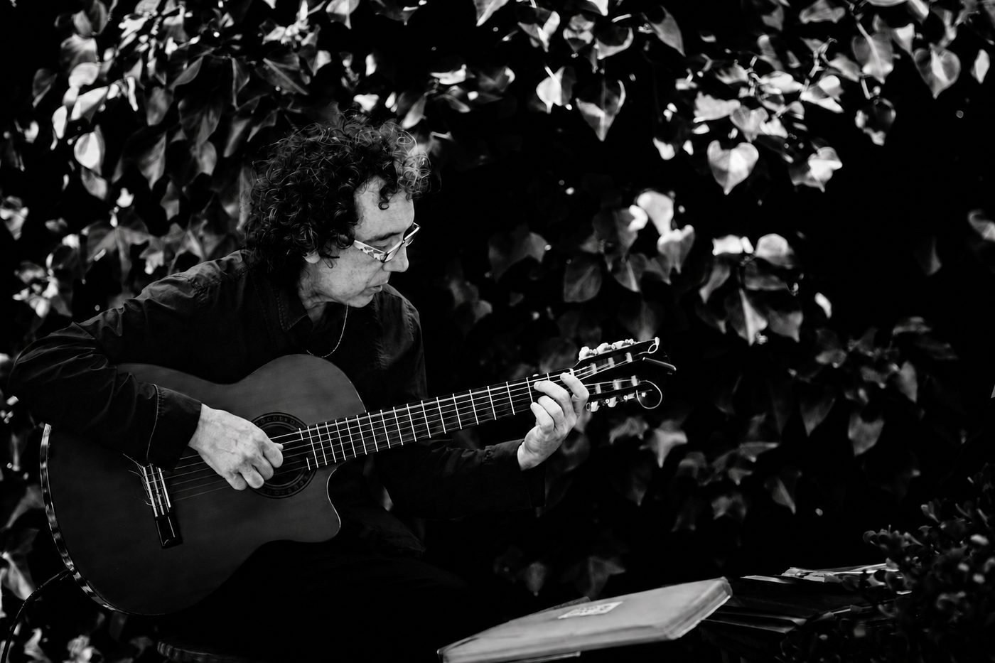 Miguel Anda tocando la guitarra en un jardín, rodeado de hiedra, en blanco y negro